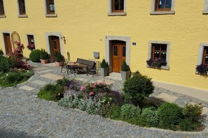 A yellow building with a paved courtyard, outdoor seating, and potted plants. - Holiday apartment with 3 bedrooms (Weißenstadt)