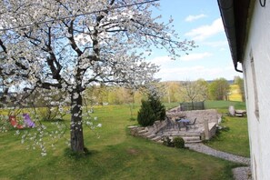 Ein Garten mit einem blühenden Baum, einer Steinsitzbank und einem kleinen Tisch mit Stühlen.