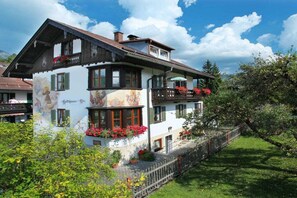 Un bâtiment de style alpin traditionnel, doté d’un balcon, d’un jardin fleuri et surplombant un ciel dégagé.