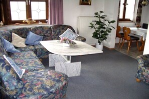 A living room with a floral sofa, a marble coffee table, and a dining area with wooden chairs and a table. - Holiday apartment with 1 bedroom (Garmisch-Partenkirchen)