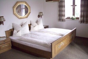 A bedroom with a wooden bed, a nightstand, a mirror, and a window with curtains. - Holiday apartment with 1 bedroom (Garmisch-Partenkirchen)