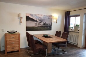 Ein Essbereich mit Holztisch, vier Stühlen, einer Anrichte und einem großen Landschaftsbild.