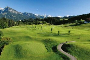 Ein Golfplatz mit gewundenem Weg, umgeben von Bäumen und Bergen.