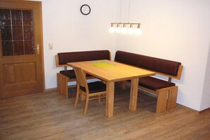 Ein Zimmer mit einem Holztisch, Bänken, einer Wanduhr und einer Tür mit Glasfenster.