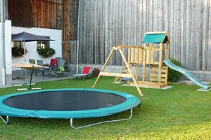 Ein Garten mit Trampolin, Holzschaukel und Rutsche.