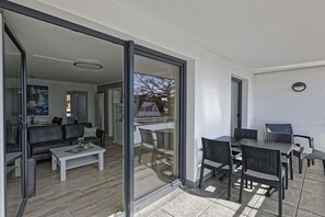 Ein modernes Wohnzimmer mit einer Couch, einem Couchtisch und Glastüren, die auf einen Balkon mit Gartenmöbeln führen.