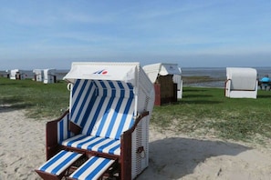 A beach chair with a striped cushion, a covered wicker chair, and a small covered structure in the background. - Pearl at the marina, Pfahlhaus Harlesiel (Carolinensiel-Harlesiel)