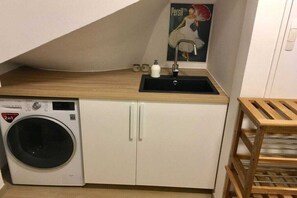A compact laundry area with a washing machine, a sink, and a poster on the wall. - Pearl at the marina, Pfahlhaus Harlesiel (Carolinensiel-Harlesiel)
