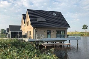 A modern house with a flat roof, large windows, and a dock extending into a body of water. - Pearl at the marina, Pfahlhaus Harlesiel (Carolinensiel-Harlesiel)