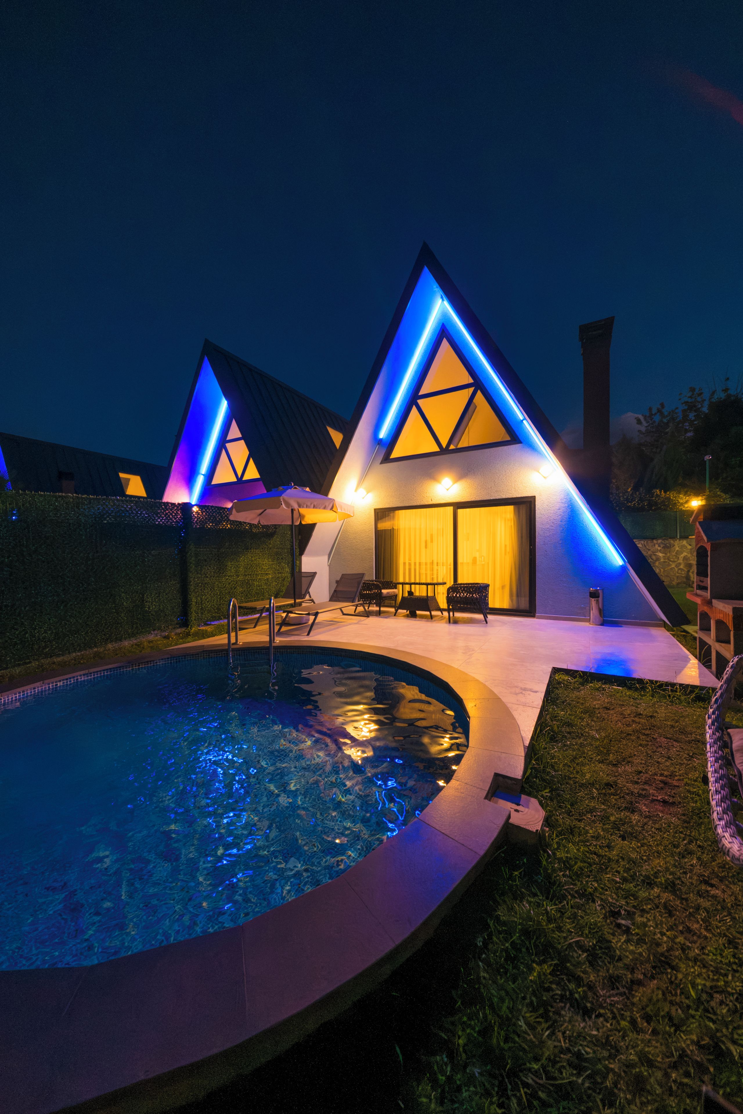 A modern building with a pool, outdoor seating, and a well-lit facade.