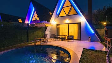 Un edificio moderno con piscina, zona de estar exterior e iluminación destacada en la fachada.