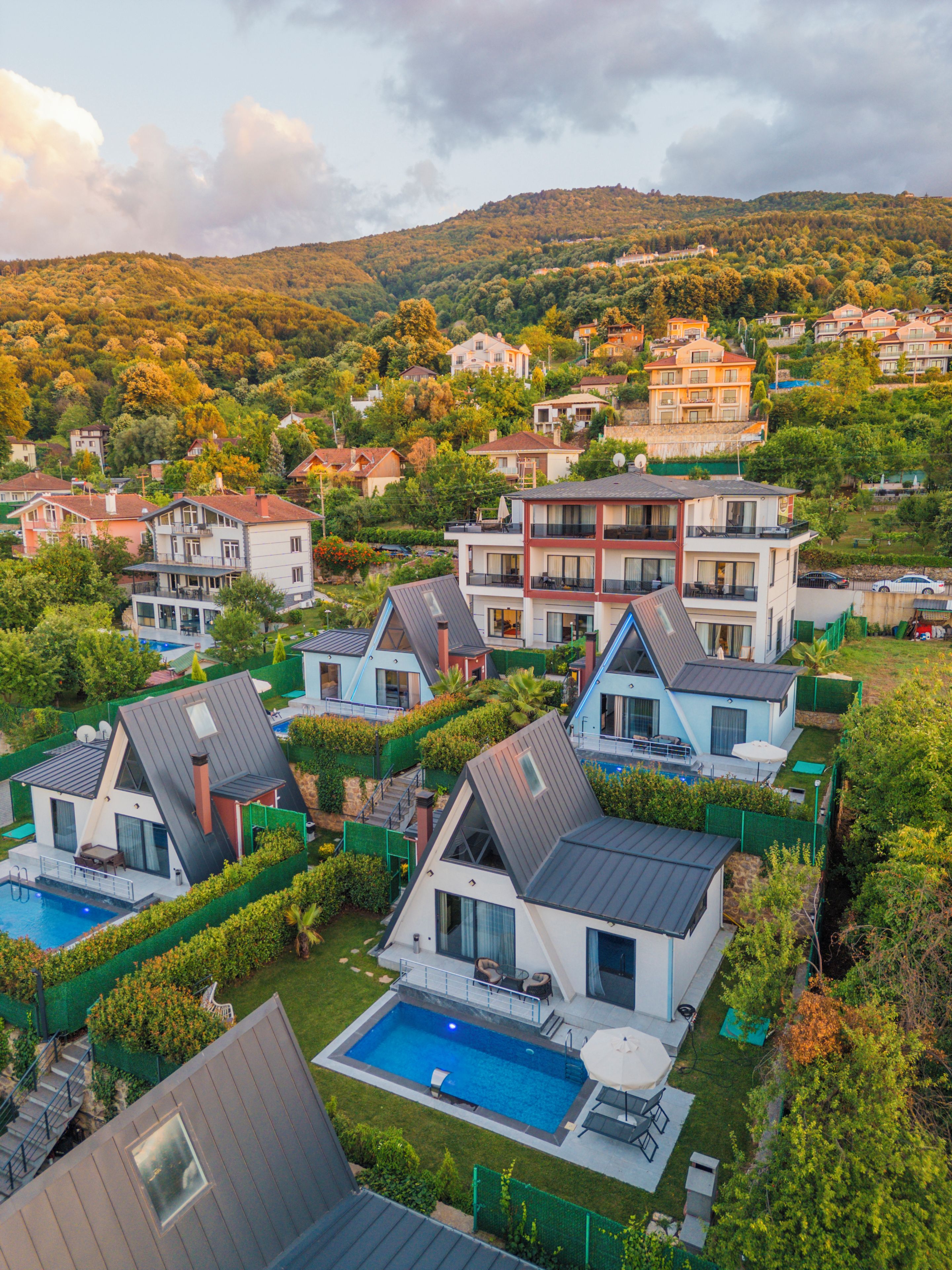 A residential area with modern houses, a swimming pool, and a hilly backdrop.