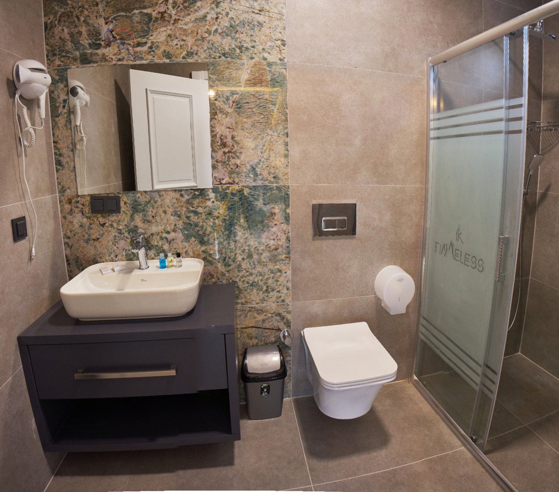 Un baño con lavamanos, espejo, dispensador de toallas, inodoro y zona de ducha.