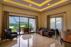 A spacious living room with a large sliding glass door leading to a patio area, furnished with a sofa, chairs, and a small table.