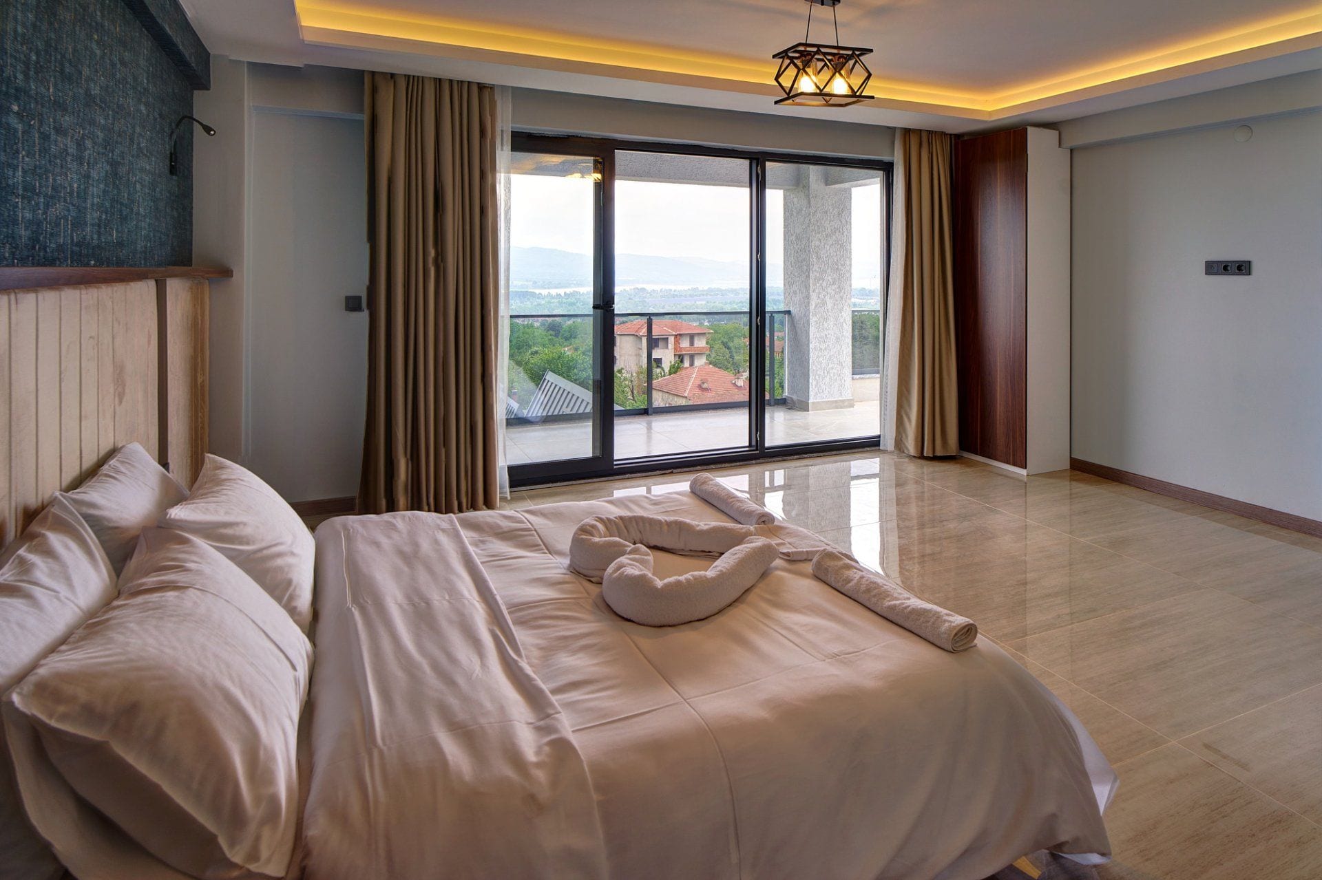 Une chambre d’hôtel avec un grand lit, une vue dégagée sur l’extérieur grâce à une porte-fenêtre coulissante et un luminaire moderne au plafond.