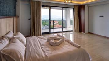 Une chambre d’hôtel avec un grand lit, une vue dégagée sur l’extérieur grâce à une porte-fenêtre coulissante et un luminaire moderne au plafond.