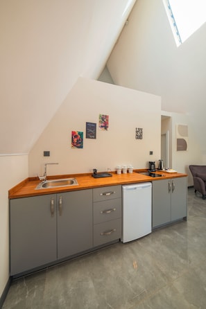 A modern kitchen with grey cabinets, a wooden countertop, a dishwasher, and a coffee maker. There are three wall art pieces and a motivational quote on the wall.