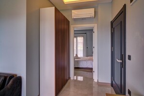A hallway with a bed in the background, an air conditioning unit, and a door on the right.
