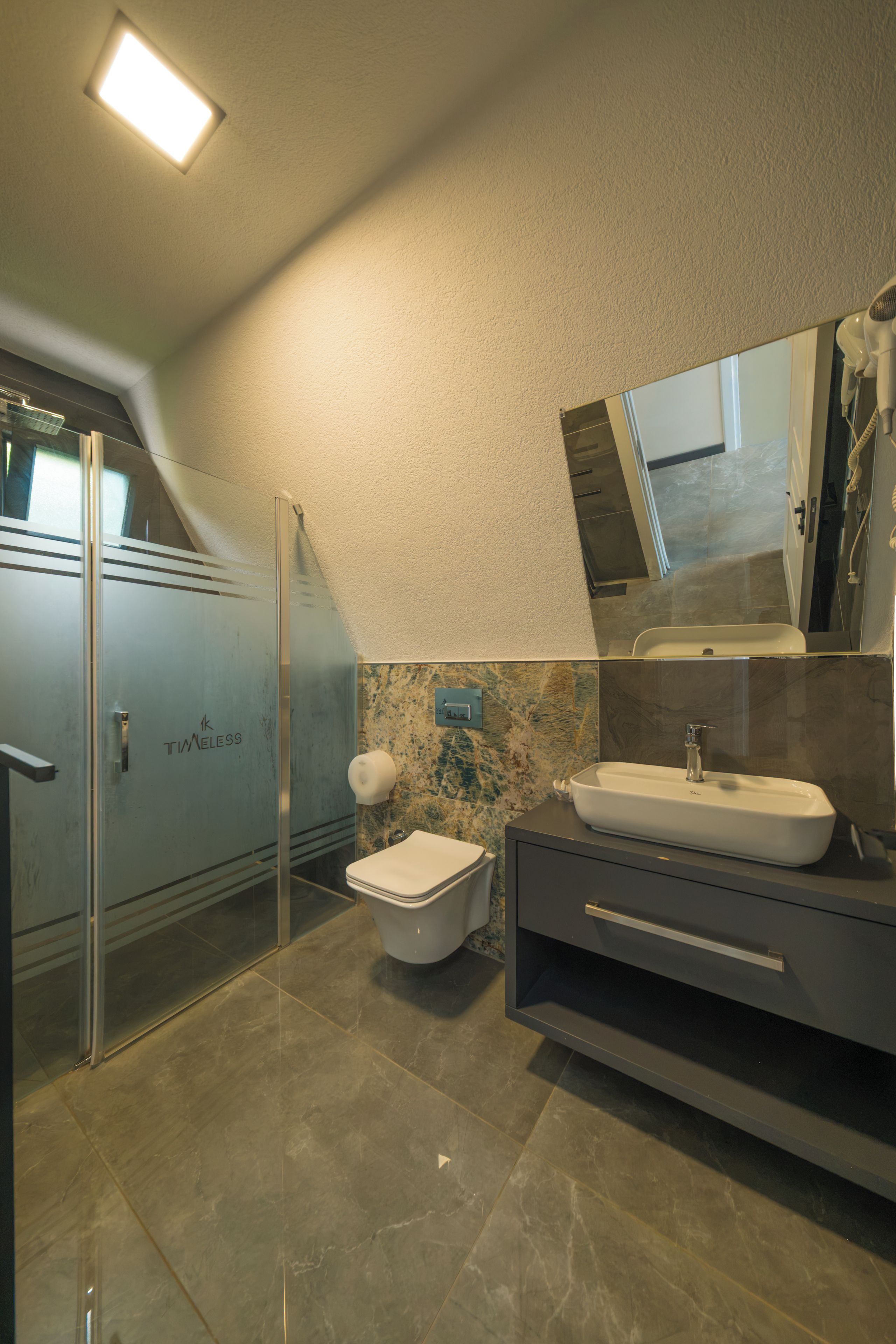 Un baño moderno con cabina de ducha de vidrio, inodoro, lavamanos y tocador con espejo.