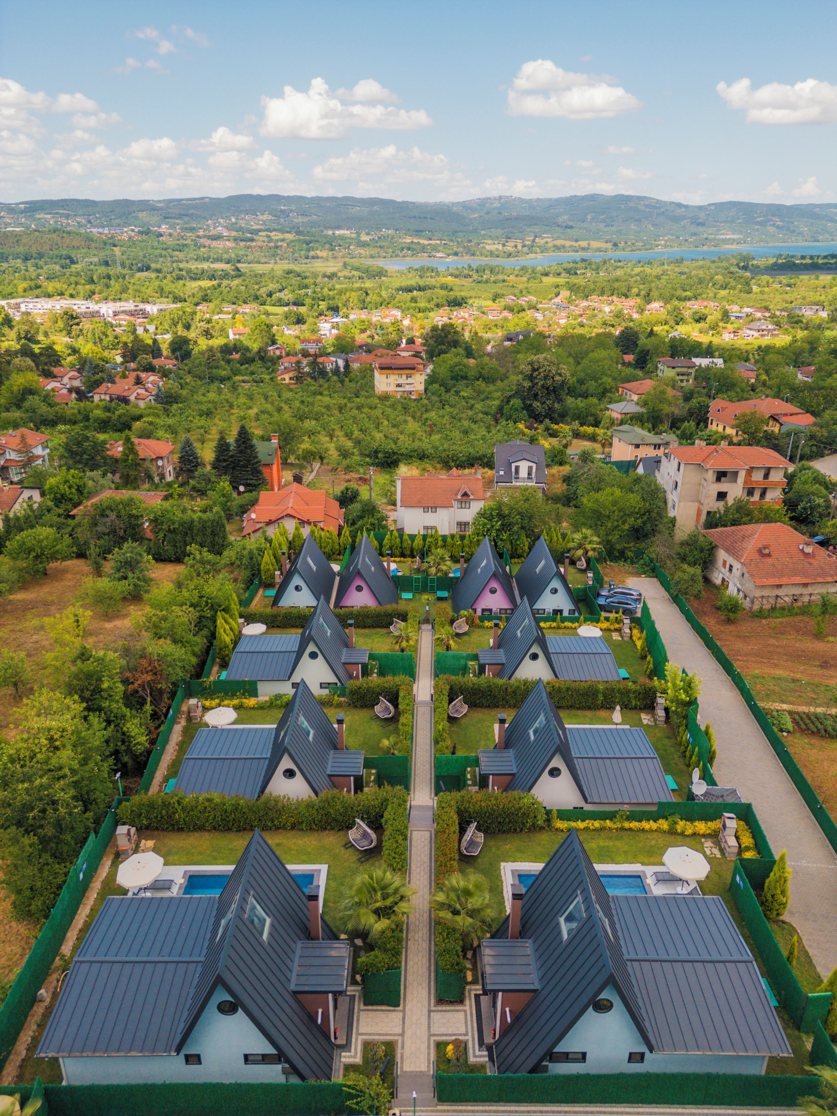 A residential area with multiple houses, a central pathway, and a distant view of a lake and hills.