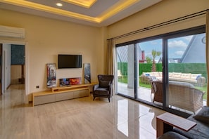 Amplia sala de estar con televisor de pantalla plana, obras de arte, un sillón cómodo, un sofá y un gran ventanal corredero que da a un espacio exterior.