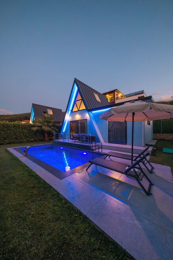 A modern house with a swimming pool, a patio with lounge chairs, and a well-maintained lawn.