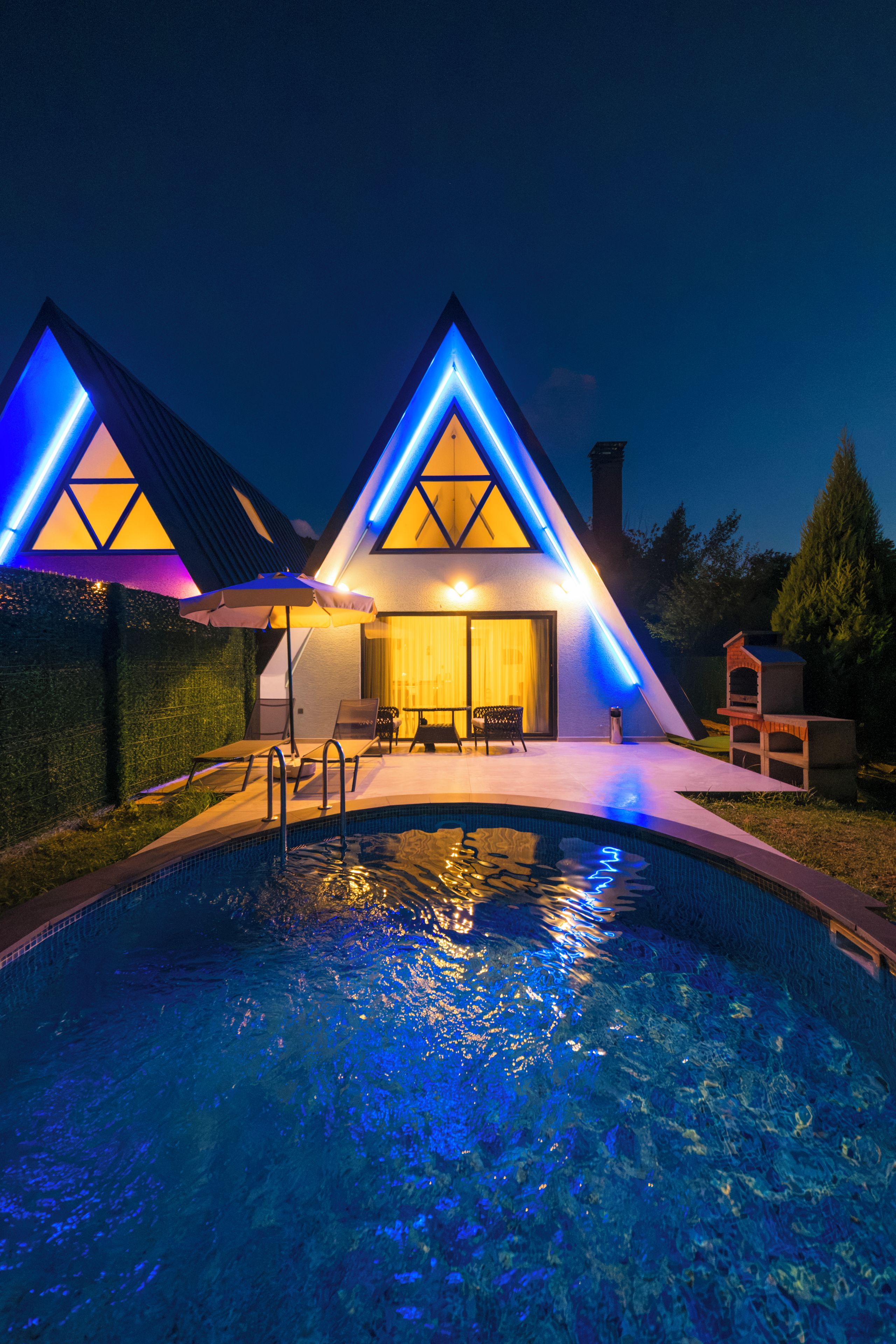 Un edificio moderno con piscina, que destaca por su diseño de techo triangular e iluminación azul.