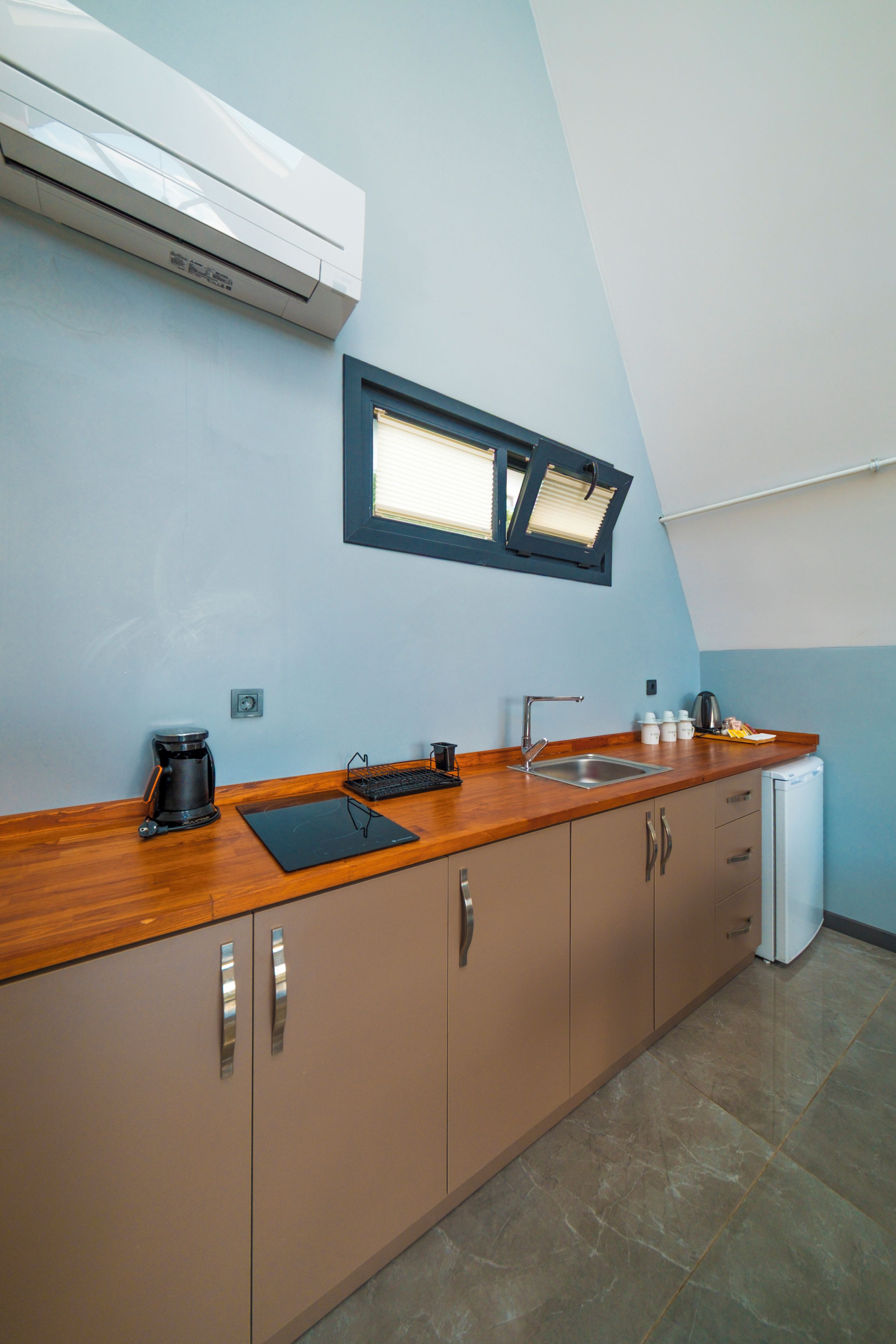 Eine Küche mit Backofen, Kaffeemaschine, Spüle und einem Fenster mit Jalousien.