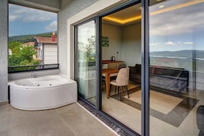 Un baño moderno con una bañera independiente, un balcón con cerramiento de vidrio que tiene una zona de comedor y vistas a un paisaje montañoso.