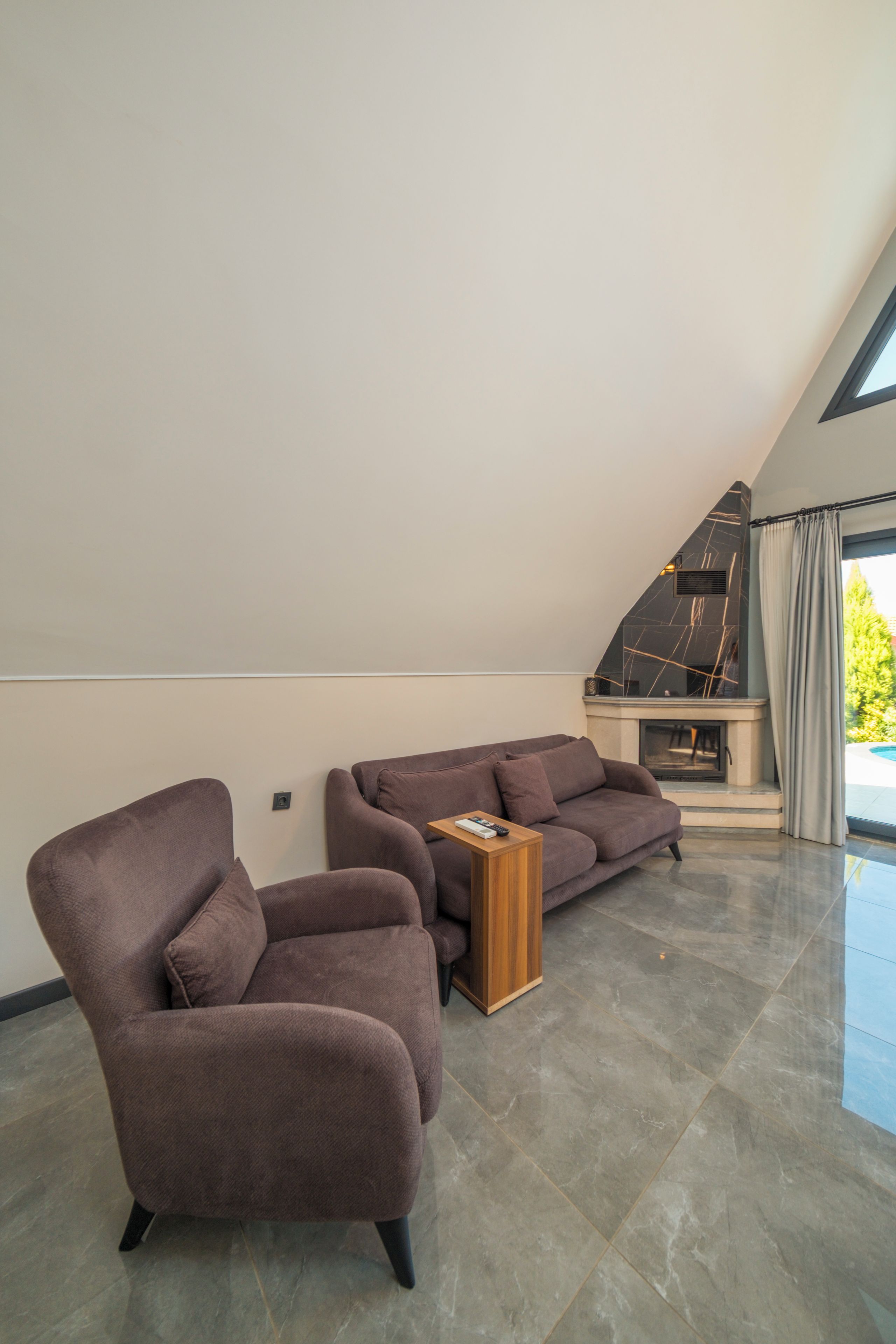 Una sala de estar moderna con techo inclinado, chimenea y un ventanal grande.