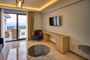 A modern hotel room with a balcony, a flat-screen TV, a sofa, a coffee table, and a desk.