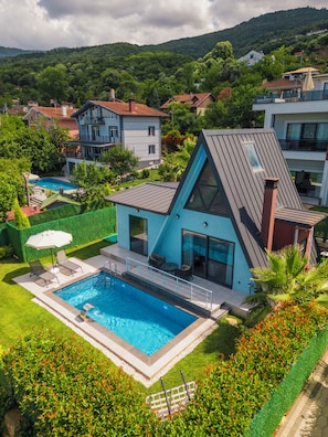 A modern house with a swimming pool, surrounded by lush greenery and hills.