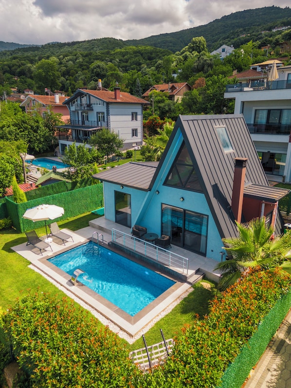 A modern house with a swimming pool, surrounded by lush greenery and hills.