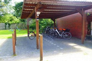 Ein überdachter Fahrradstellplatz mit Backsteinmauer und einer Holzpergola.