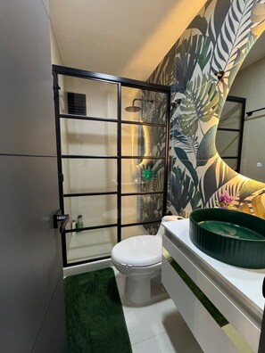 A bathroom with a toilet, a shower enclosure, and a sink with a green basin. - Fontana Country Set (Ibagué)