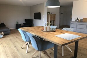 A modern living space with a wooden dining table, blue chairs, a grey sofa, and a television mounted on the wall. - Holiday apartment with 2 bedrooms (Mehring, Deutschland)