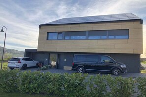 A modern two-story building with a flat roof, a garage, and a driveway with two cars parked. - Holiday apartment with 2 bedrooms (Mehring, Deutschland)