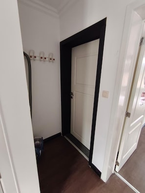 A hallway with a white door, a black trim, and a white wall with a light switch. - Studio centrum (Leuven)
