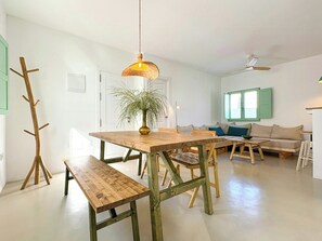 Ein geräumiger Wohnbereich mit Holztisch, Bänken, einer Couch und einem Deckenventilator.