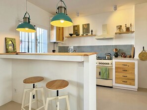 A kitchen with a central island, two stools, pendant lights, and a stove. - Charming Artisanal Home in Vejer de la Frontera (Vejer de la Frontera)