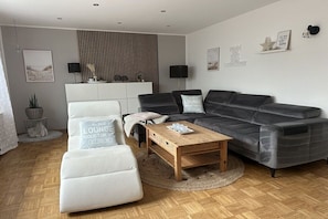 A modern living room with a grey sofa, white armchairs, a wooden coffee table, and a white cabinet. - Holiday home with 4 bedrooms (Wangerland)