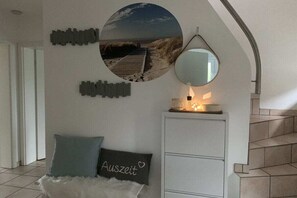 A room with a bed, a bedside table with a lamp, a wall-mounted mirror, and a circular picture of a beach. - Holiday home with 4 bedrooms (Wangerland)