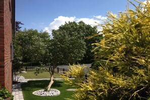 A landscaped garden with a tree, a circular stone feature, and a brick building. - Holiday home with 4 bedrooms (Wangerland)