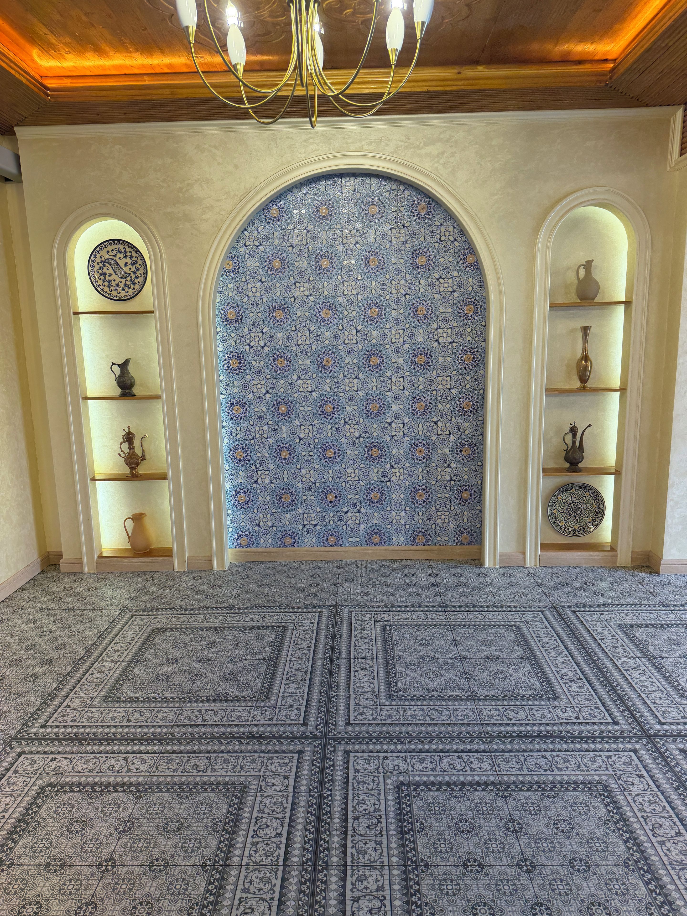 Une pièce dotée d’un tapis à motifs, d’un lustre et d’étagères ornées d’objets décoratifs.