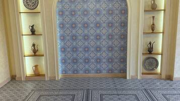 Une pièce dotée d’un tapis à motifs, d’un lustre et d’étagères ornées d’objets décoratifs.