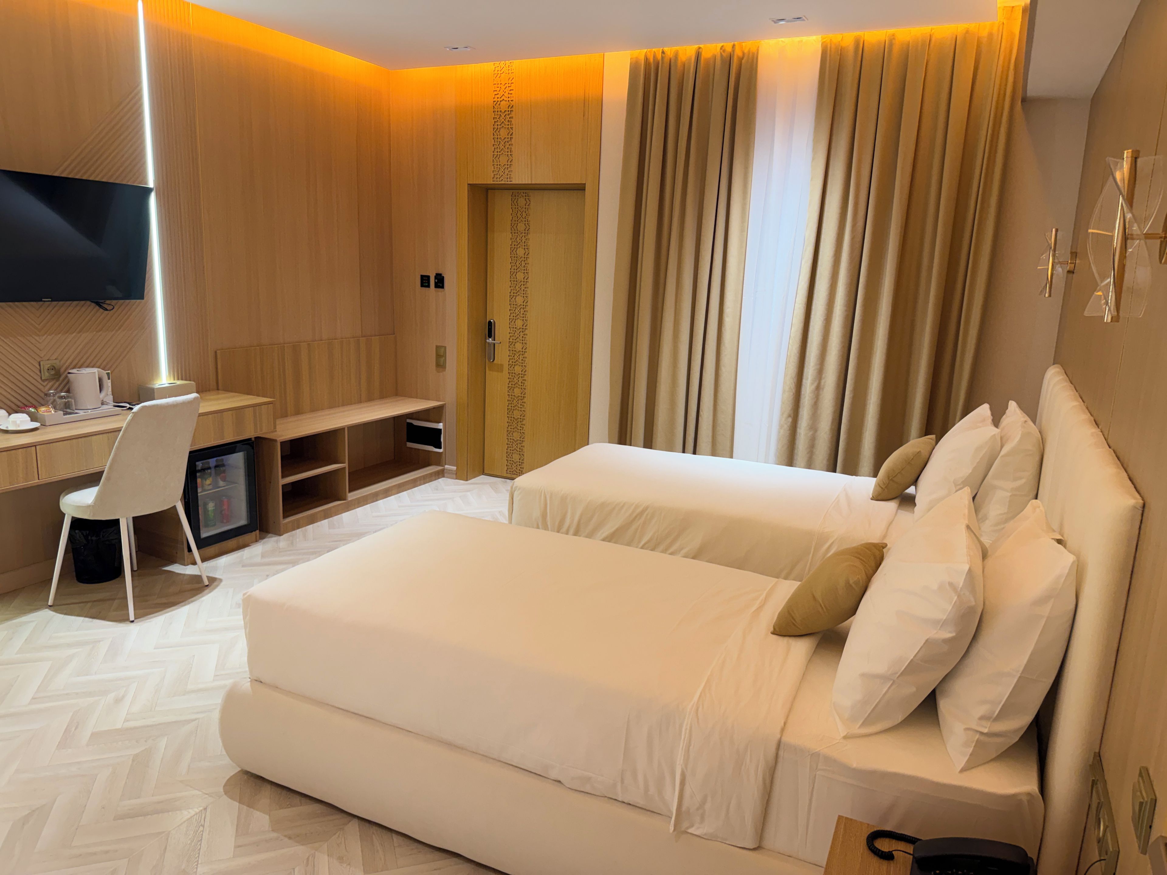 A hotel room with a bed, a desk, a chair, a television, and a minibar.