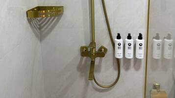 Eine Dusche mit goldfarbenen Armaturen, einem Handbrausekopf und einem an der Wand montierten Bedienfeld mit Pflegeprodukten.