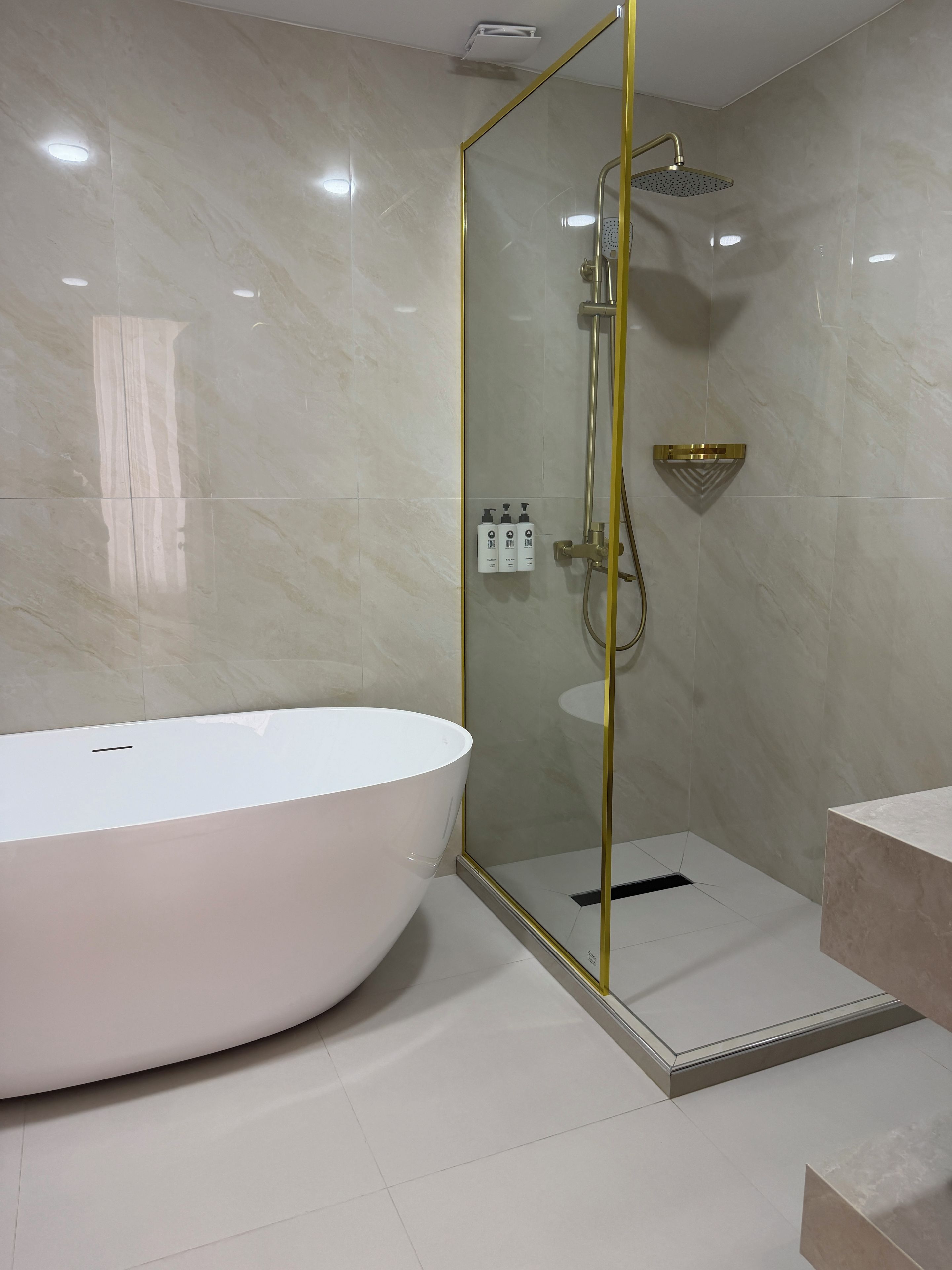 A modern bathroom with a freestanding bathtub, a glass-enclosed shower, and a gold-framed mirror.