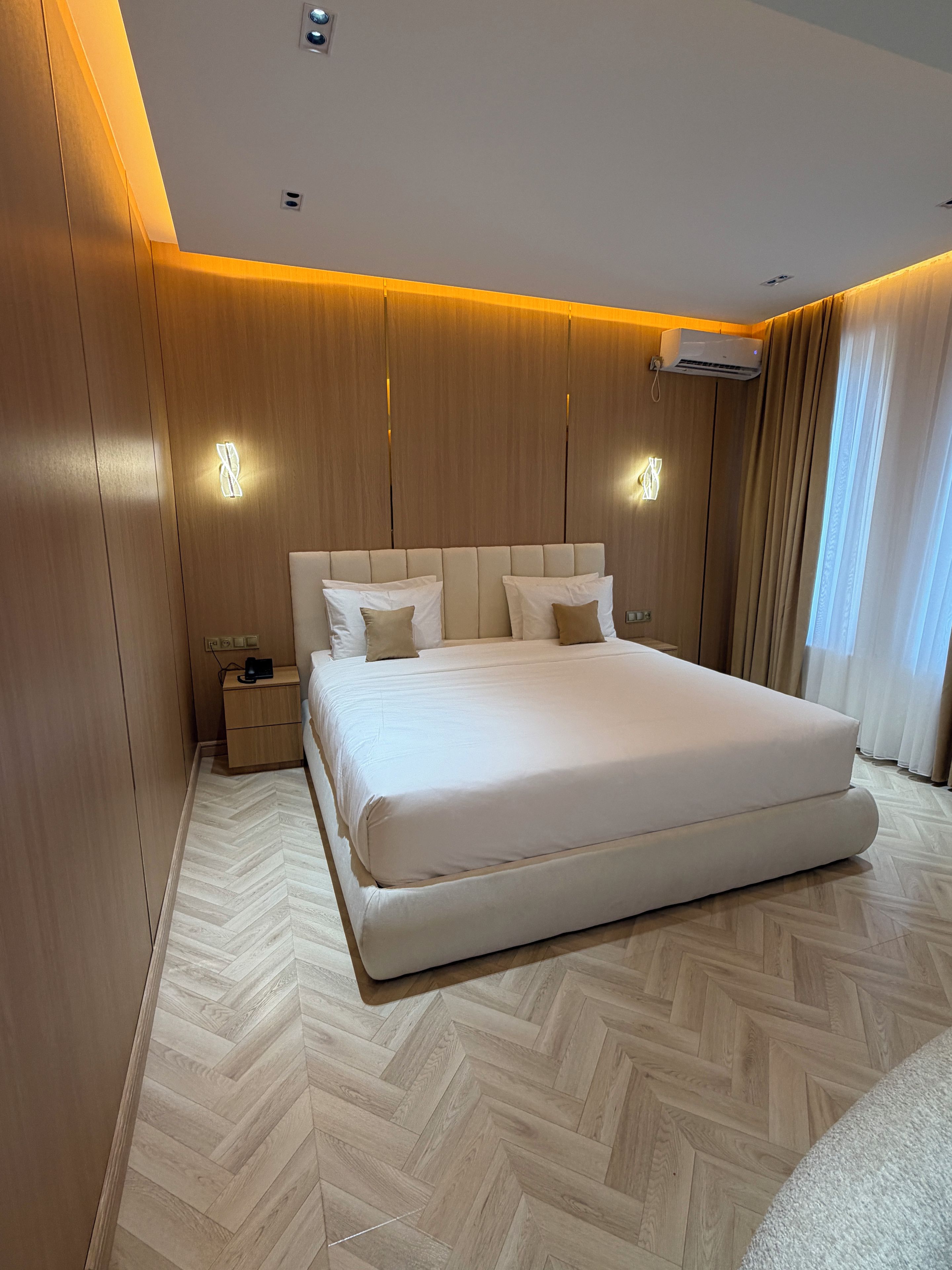 Ein modernes Schlafzimmer mit einem großen Bett, Holzwandverkleidungen und einem Fischgrätparkett.