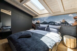 Ein Schlafzimmer mit Oberlicht, einem Bett mit dunkler Bettwäsche, einem grauen Sofa und einer Wandmalerei.